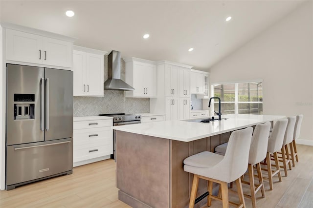 kitchen with light wood-style floors, wall chimney exhaust hood, stainless steel appliances, white cabinetry, and tasteful backsplash