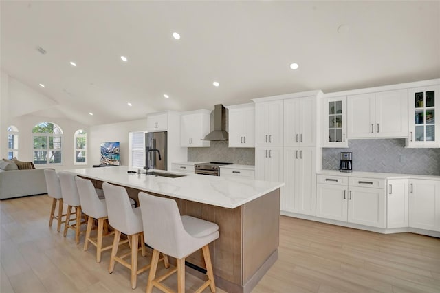 kitchen with wall chimney range hood, appliances with stainless steel finishes, a breakfast bar area, backsplash, and vaulted ceiling
