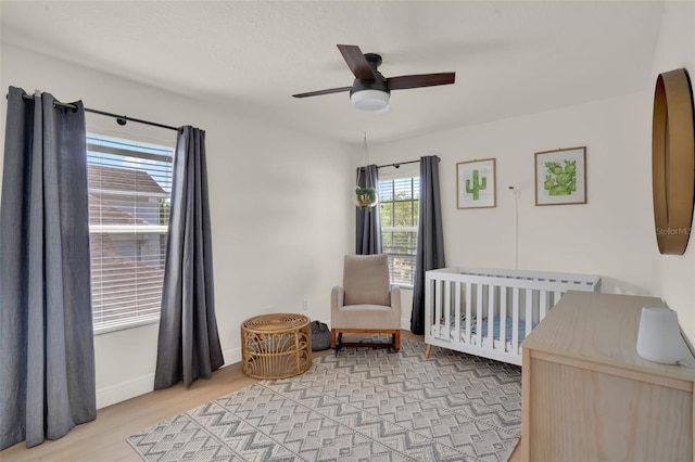 bedroom featuring a nursery area, baseboards, a ceiling fan, and light wood-type flooring