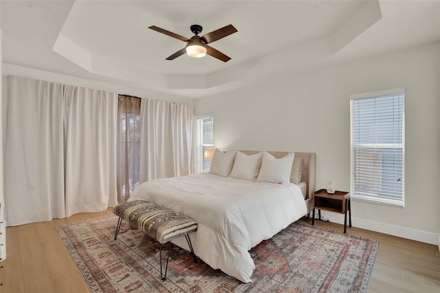 bedroom featuring a ceiling fan, baseboards, a raised ceiling, and light wood-type flooring