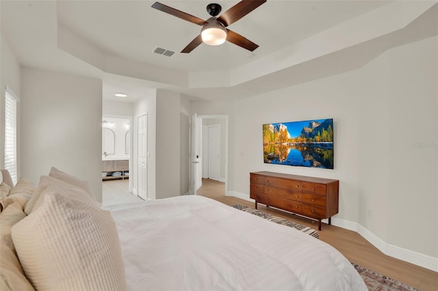 bedroom with visible vents, baseboards, connected bathroom, a tray ceiling, and light wood-style flooring