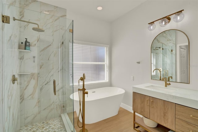 bathroom with wood finished floors, baseboards, vanity, a marble finish shower, and a soaking tub