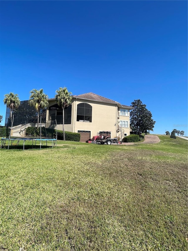 back of house featuring a lawn, a trampoline, and stucco siding