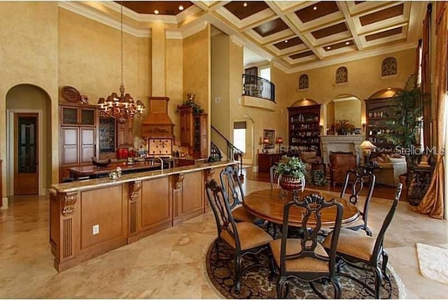 dining space with crown molding, arched walkways, a chandelier, a high ceiling, and coffered ceiling