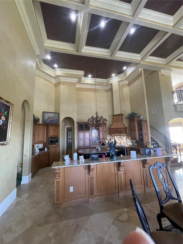 kitchen featuring brown cabinets, arched walkways, a chandelier, and a towering ceiling
