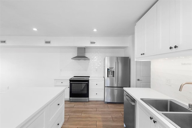 kitchen with visible vents, a sink, wall chimney exhaust hood, light wood-style floors, and appliances with stainless steel finishes