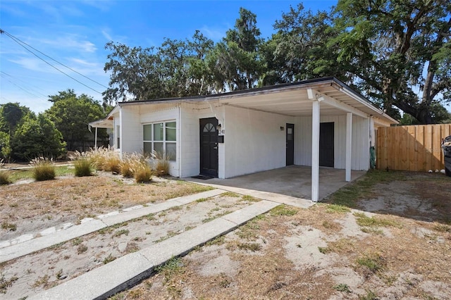 view of front of home featuring dirt driveway, fence, an attached carport, and concrete block siding