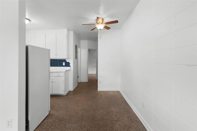 hallway featuring dark colored carpet and baseboards