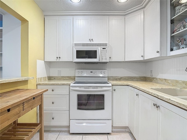 kitchen featuring a sink, light tile patterned floors, white cabinets, and white appliances