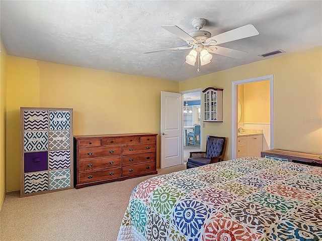 carpeted bedroom with a ceiling fan, visible vents, and ensuite bath