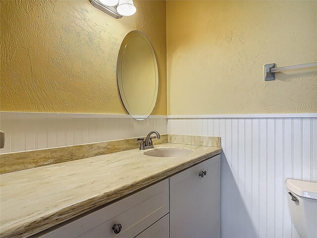 half bath featuring vanity, a wainscoted wall, and toilet