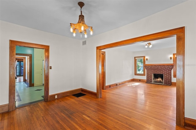 806 E Amelia St, Orlando, FL 32803 - unfurnished living room featuring hardwood / wood-style flooring, baseboards, visible vents, a brick fireplace, and a notable chandelier