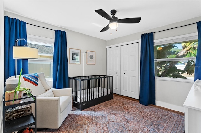 bedroom featuring a nursery area, ceiling fan, baseboards, wood finished floors, and a closet