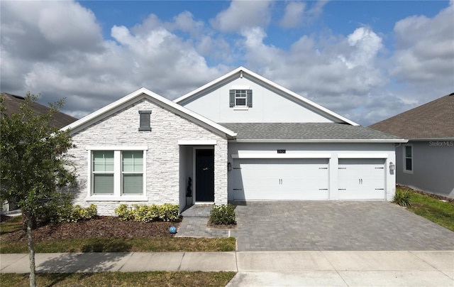 view of front of home with decorative driveway, an attached garage, a shingled roof, stone siding, and stucco siding