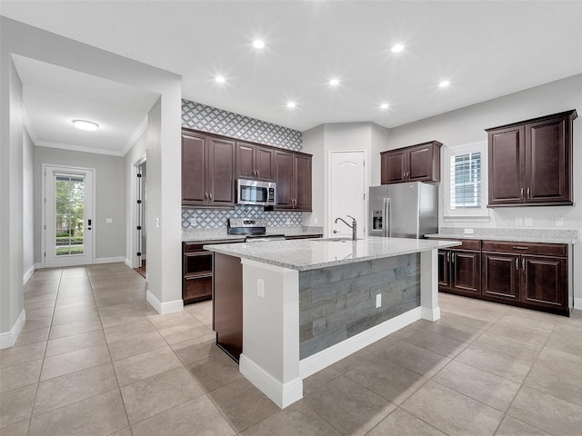 kitchen with crown molding, dark brown cabinets, stainless steel appliances, backsplash, and a center island with sink