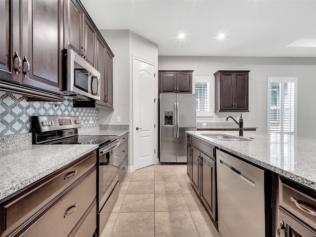 kitchen with decorative backsplash, appliances with stainless steel finishes, light stone countertops, dark brown cabinets, and a sink
