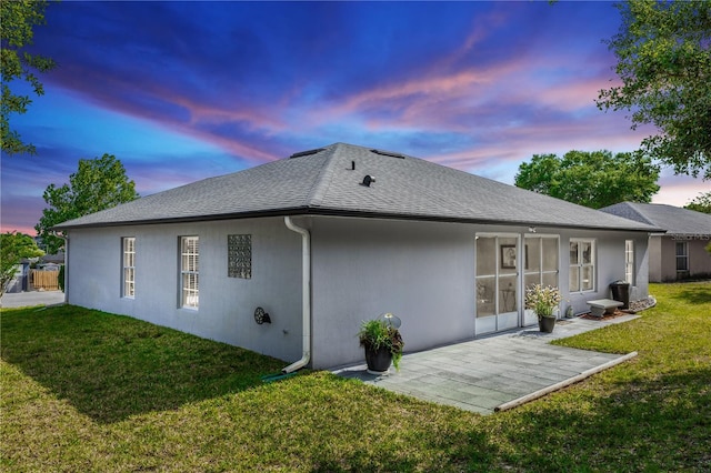 back of house with a yard, a shingled roof, a patio area, and stucco siding