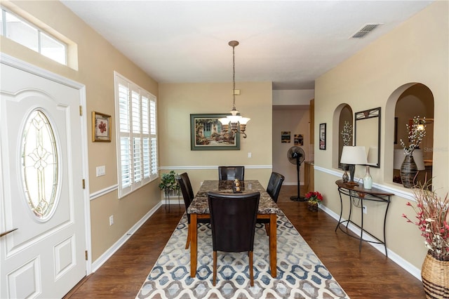 dining room with dark wood-style flooring, arched walkways, a notable chandelier, and a wealth of natural light