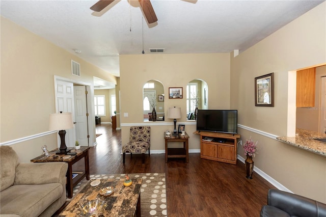 living area with dark wood-style flooring, ceiling fan, visible vents, and arched walkways