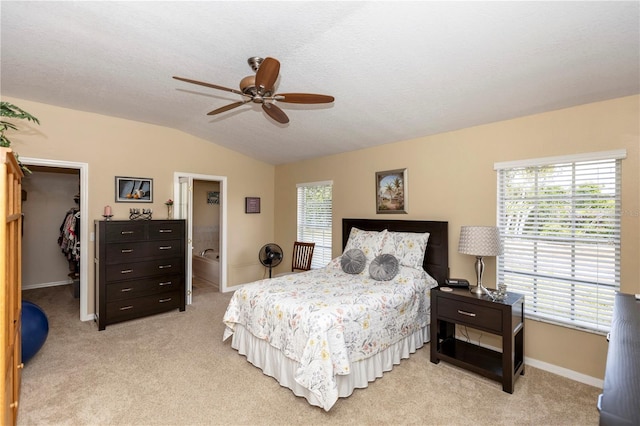 bedroom featuring a walk in closet, baseboards, vaulted ceiling, and light colored carpet