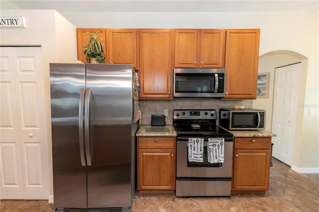 kitchen with backsplash, stainless steel appliances, arched walkways, and brown cabinets
