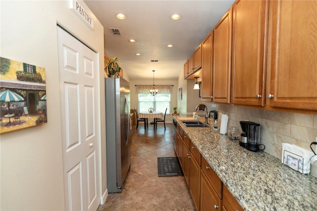 kitchen with backsplash, brown cabinets, a sink, freestanding refrigerator, and recessed lighting