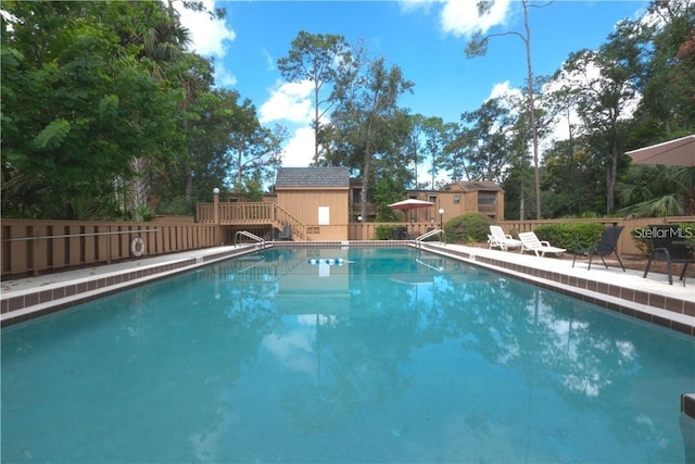 community pool featuring fence, a wooden deck, and stairs