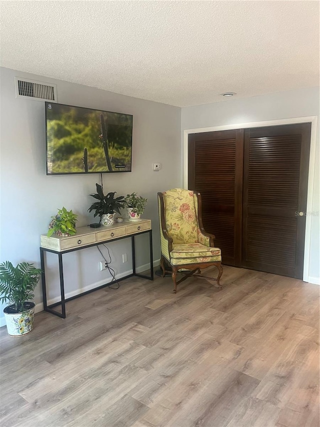 living area with baseboards, a textured ceiling, visible vents, and wood finished floors