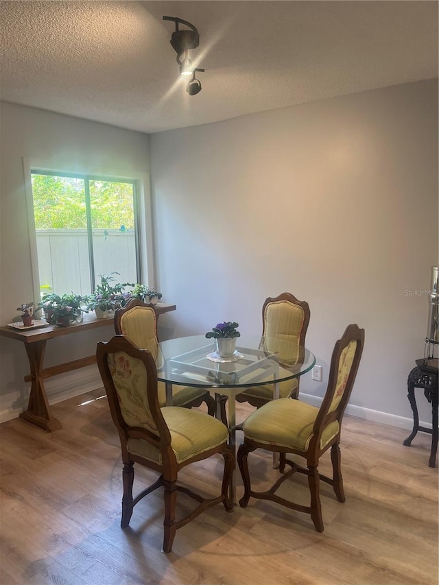 dining space featuring baseboards, a textured ceiling, and light wood-style flooring