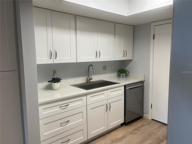 kitchen with a sink, light wood finished floors, light countertops, white cabinetry, and stainless steel dishwasher
