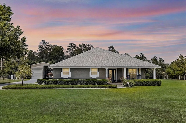 view of front of house featuring a front lawn, stucco siding, a shingled roof, a porch, and an outbuilding