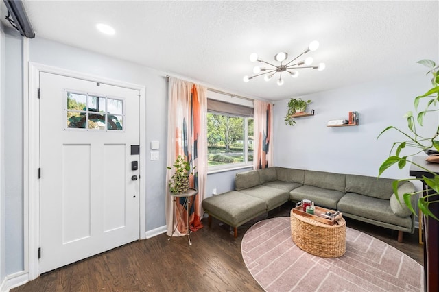 living area featuring baseboards, dark wood-type flooring, a textured ceiling, and a notable chandelier