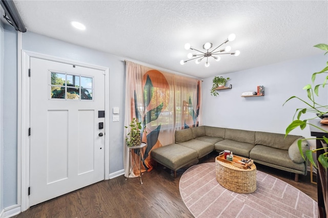 living area with an inviting chandelier, a textured ceiling, dark wood-type flooring, and baseboards