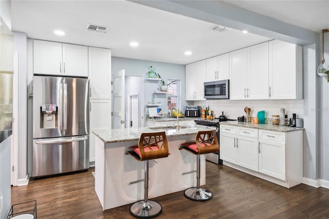 kitchen featuring dark wood-style flooring, appliances with stainless steel finishes, a sink, white cabinetry, and an island with sink