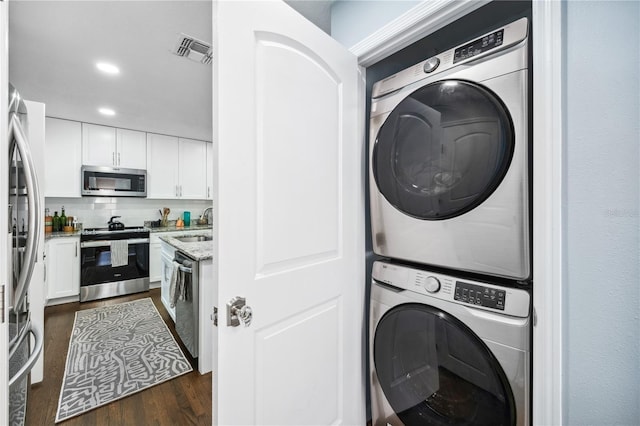 clothes washing area with laundry area, dark wood-style flooring, visible vents, stacked washer / drying machine, and a sink