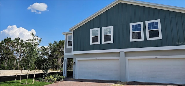view of side of property featuring board and batten siding, an attached garage, and decorative driveway