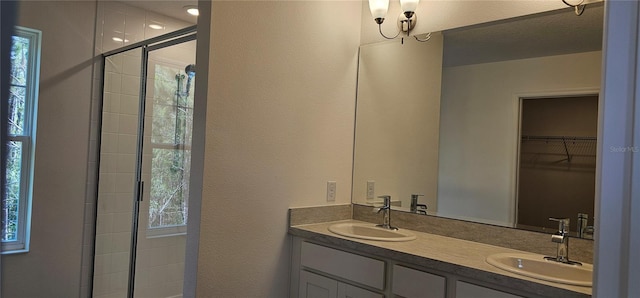 full bathroom with double vanity, a walk in closet, a sink, and a stall shower