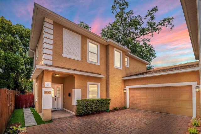multi unit property with an attached garage, decorative driveway, stucco siding, and fence