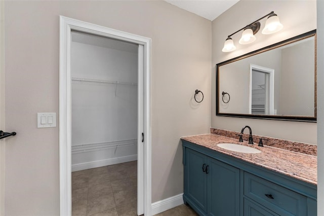 bathroom with baseboards, a walk in closet, and vanity