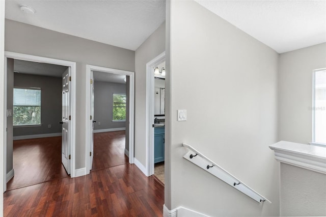 corridor featuring baseboards, dark wood-style floors, and an upstairs landing