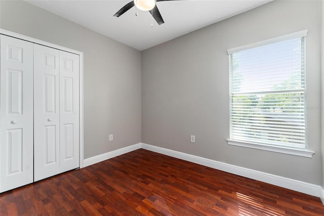 unfurnished bedroom with baseboards, a ceiling fan, dark wood finished floors, and a closet