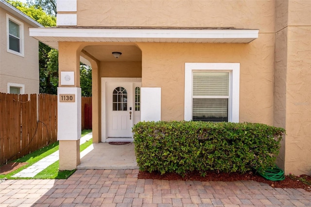 entrance to property featuring fence and stucco siding