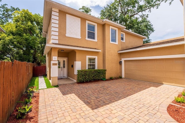view of front of home with decorative driveway, a garage, fence, and stucco siding