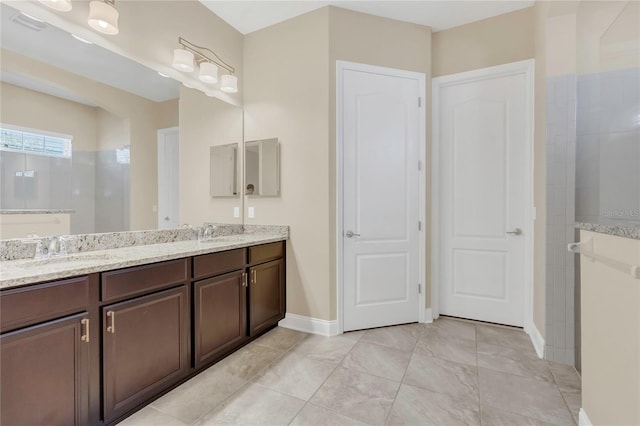bathroom featuring a sink, baseboards, double vanity, and tiled shower