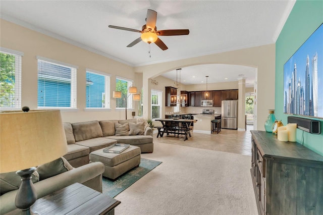 living area with crown molding, arched walkways, ceiling fan with notable chandelier, and light carpet