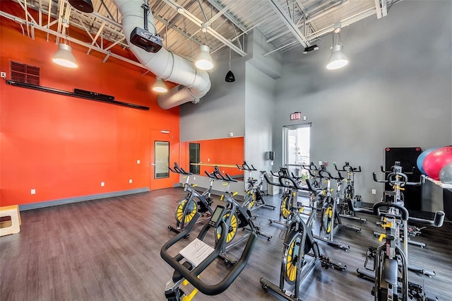 exercise room with baseboards, visible vents, wood finished floors, and a towering ceiling