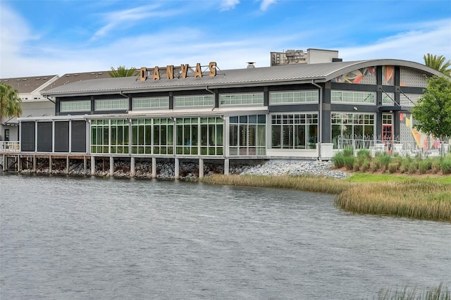 back of house featuring a water view, a standing seam roof, a chimney, and metal roof
