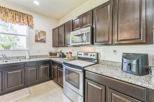2815 Shelburne Way, Saint Cloud, FL 34772 - kitchen with dark brown cabinets, light stone countertops, appliances with stainless steel finishes, a sink, and light tile patterned floors