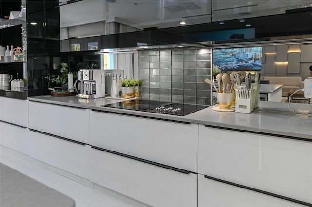 kitchen with black electric stovetop, white cabinets, modern cabinets, and tasteful backsplash