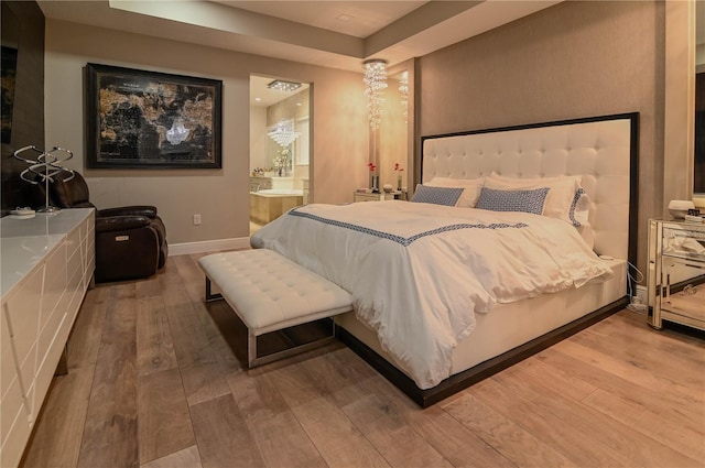 bedroom with hardwood / wood-style floors, baseboards, ensuite bathroom, and a tray ceiling